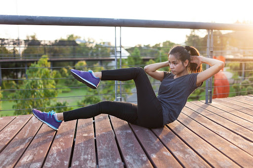 A woman performing core bodyweight exercises on a wooden deck as part of an outdoor workout routine.