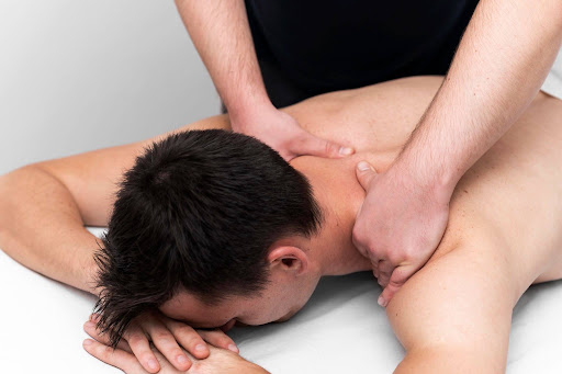 A professional massage therapist performing deep tissue massage therapy on a person's upper back to relieve chronic pain.