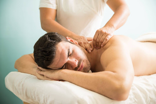 Man lying face down on a massage table receiving a shoulder and upper back massage from a professional therapist.