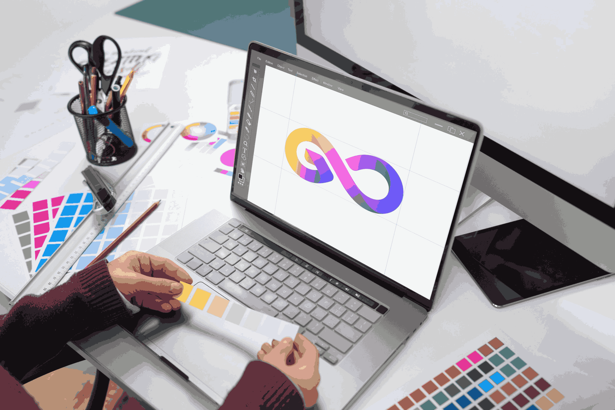 Graphic designer workstation featuring a tablet screen, color palettes, and stationery tools